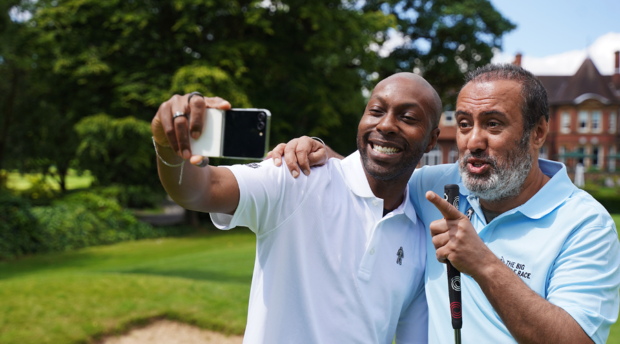 Two men smile and pose for a selfie photo on a golf course.