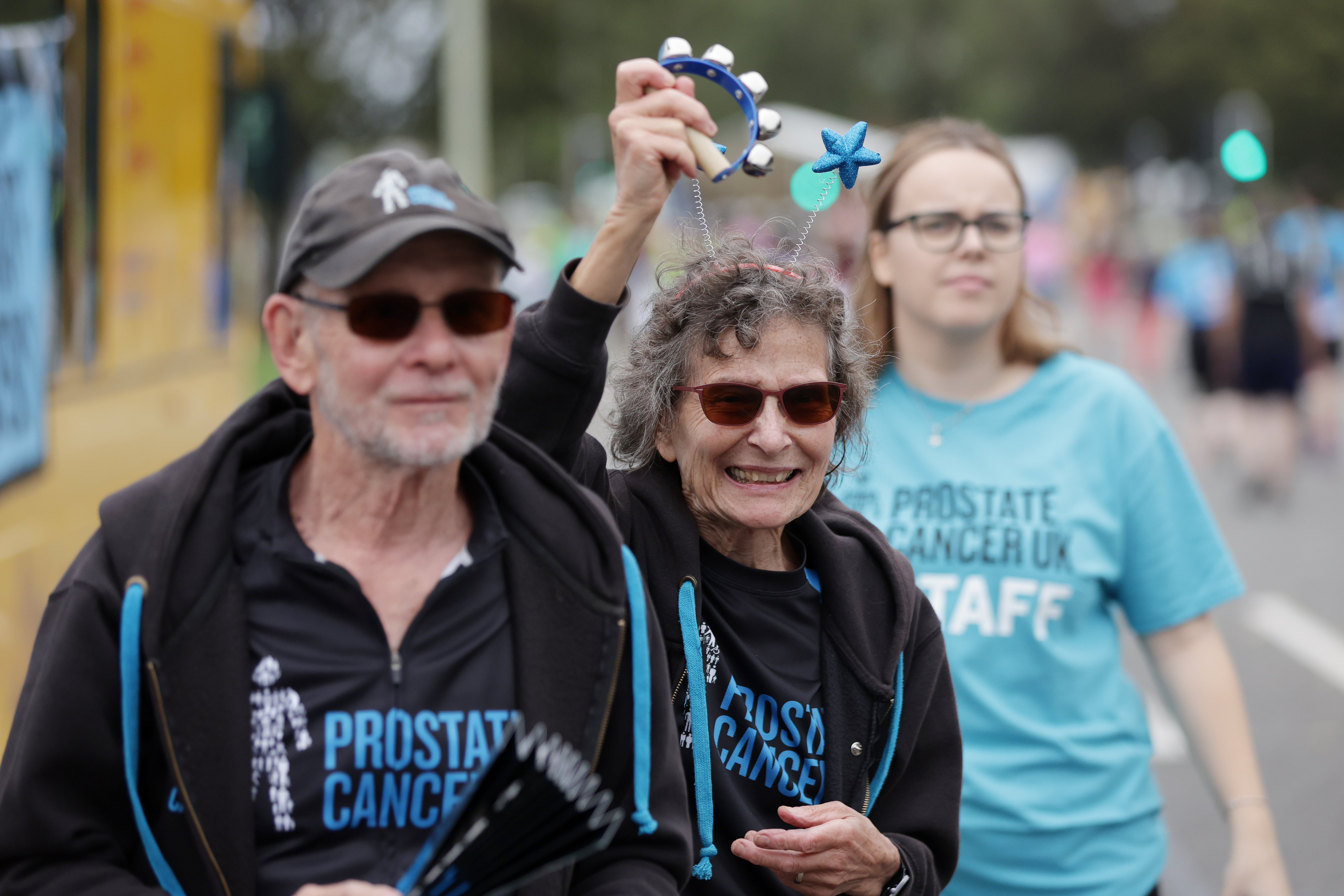 A man and woman wearing black Prostate Cancer UK t-shirts cheering at the Great North Run. 
