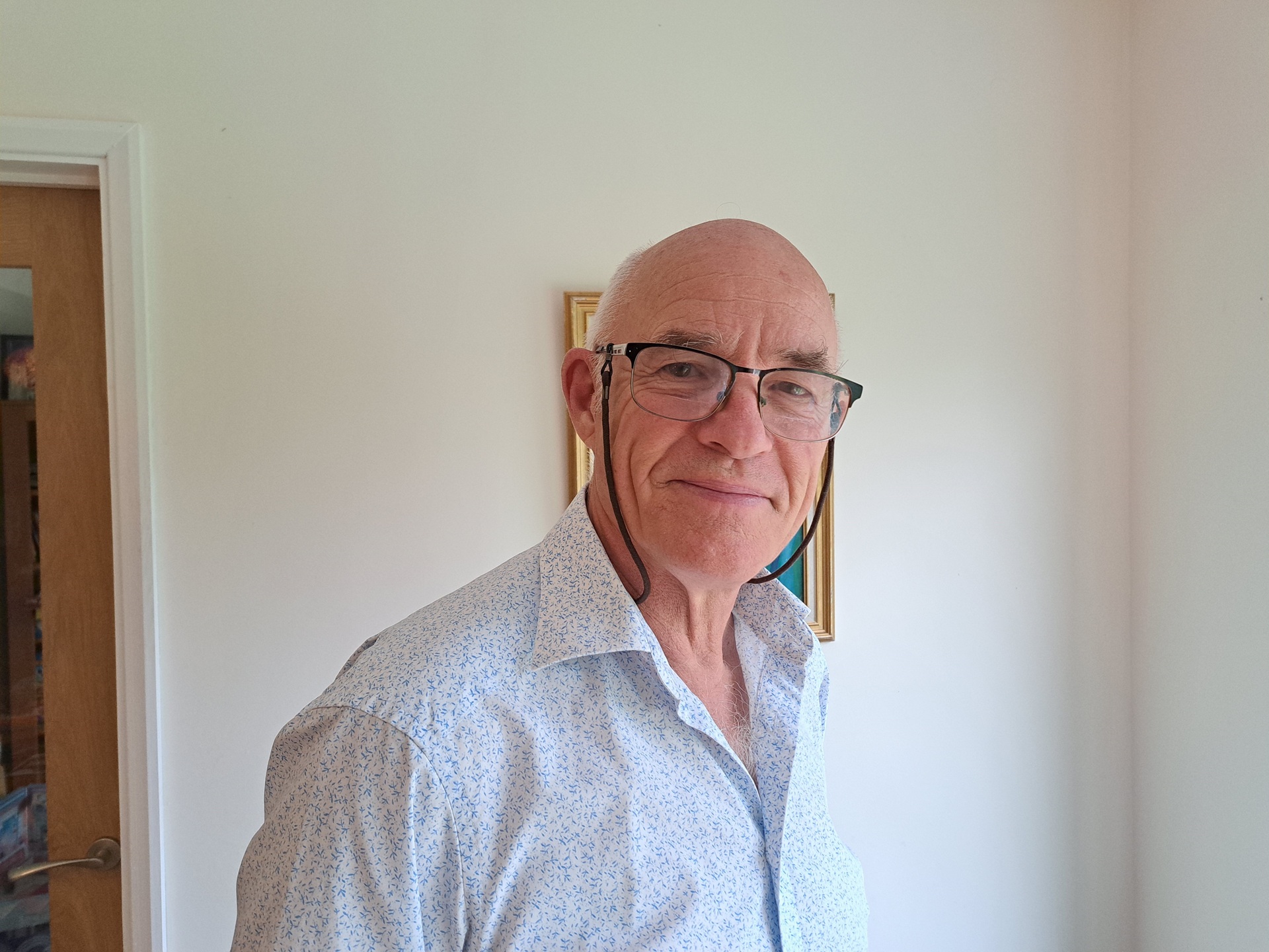 A man wearing a white shirt and glasses smiling at the camera. 