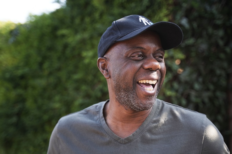 A man laughing while wearing a black cap featuring the Prostate Cancer UK logo.