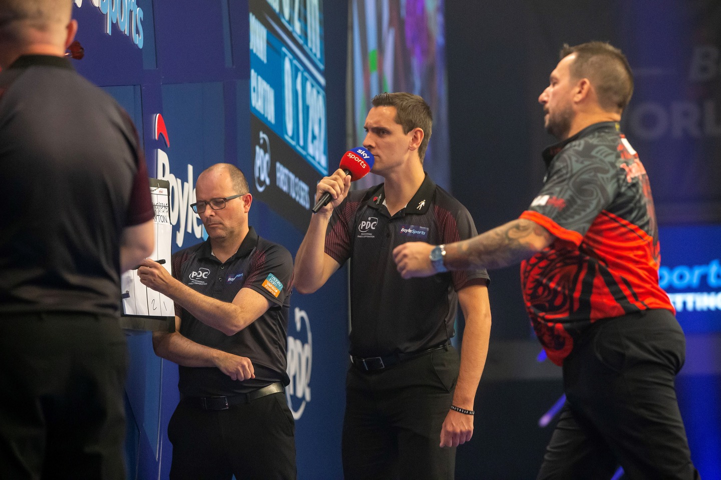 Referee Charlie Corstorphine calls out the scores alongside the oche at a darts event