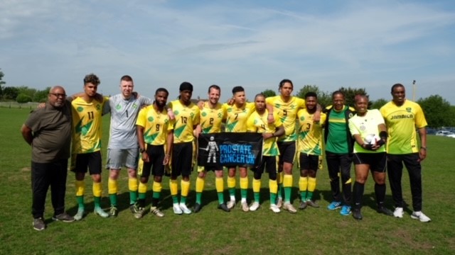 A football team standing on a pitch holding a Prostate Cancer UK banner