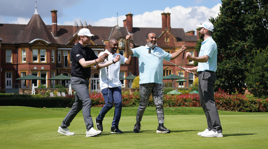 A group of four men wearing golf uniform celebrate on the green of a golf course.