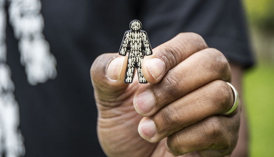 A close-up image of a hand holding up a Prostate Cancer UK Man of Men badge.