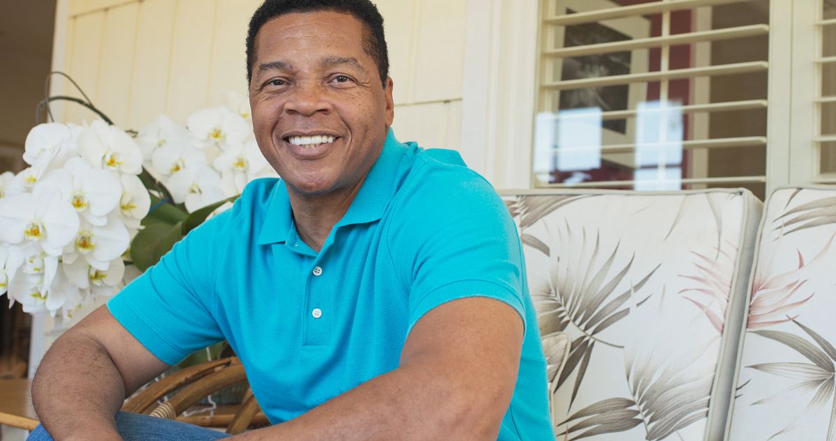 A man wearing a turquoise tee-shirt sitting on an armchair and smiling