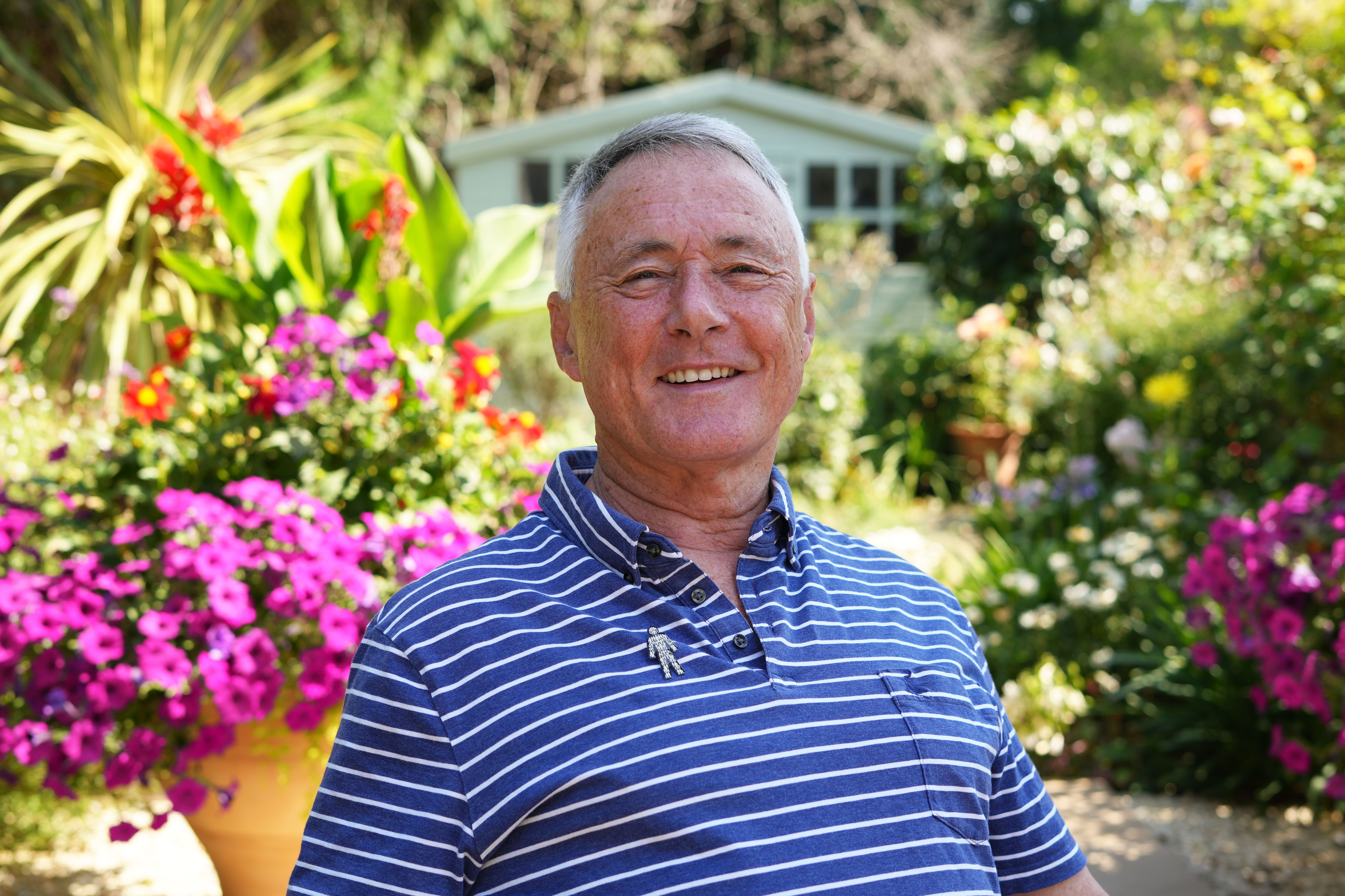 A man wearing a blue shirt sitting in a garden and smiling at the camera. 