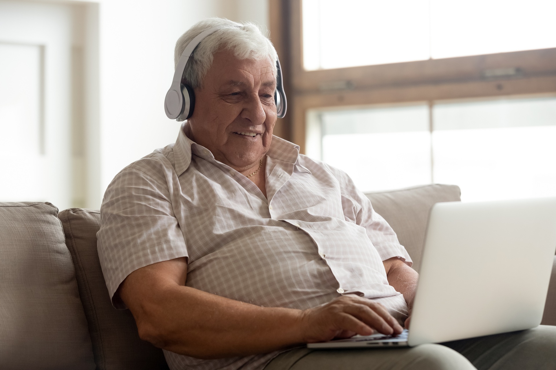 A smiling man sitting on the sofa whilst on his laptop with headphones.