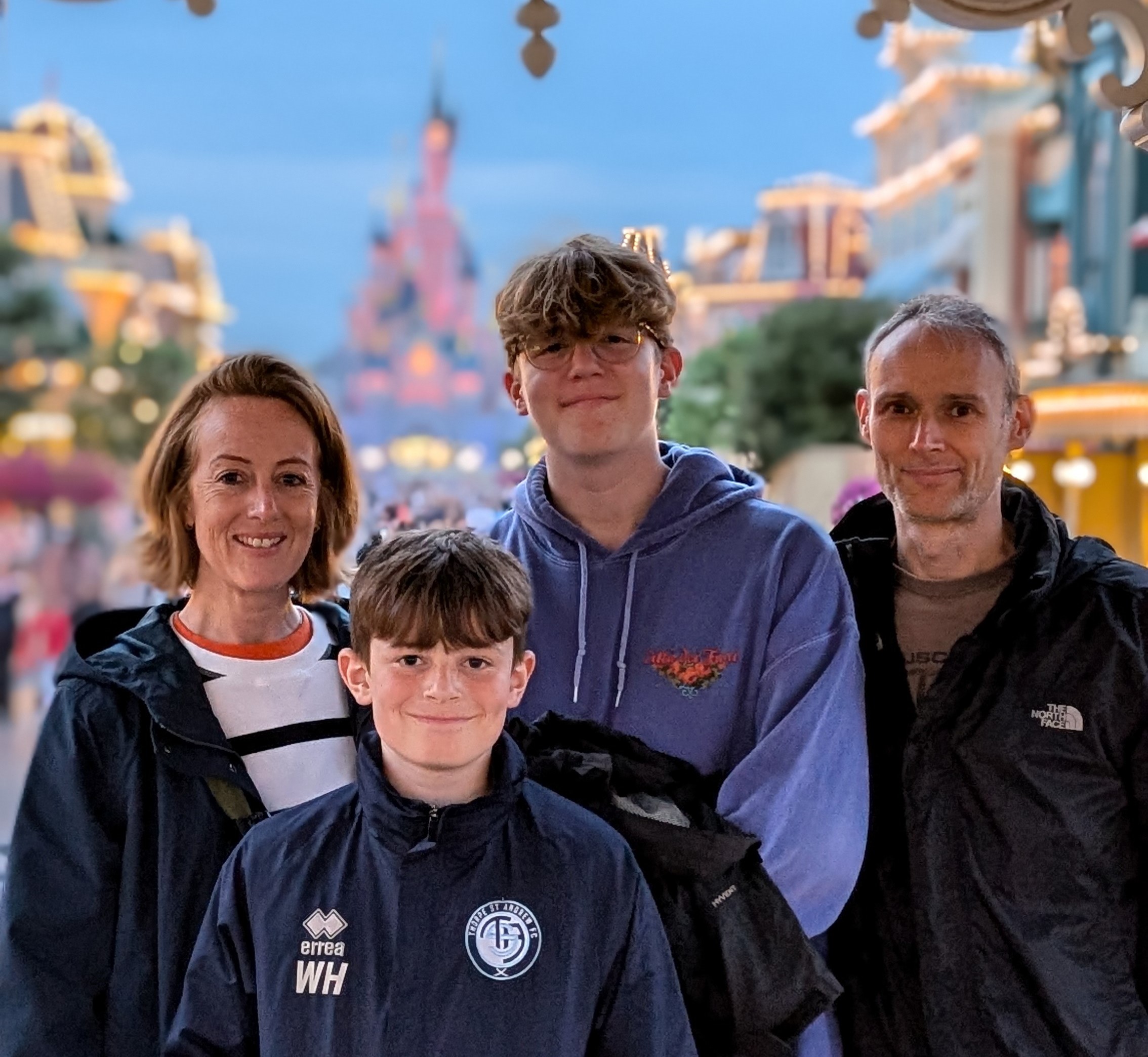 A man, woman and two boys standing together at Disneyland wearing raincoats and smiling