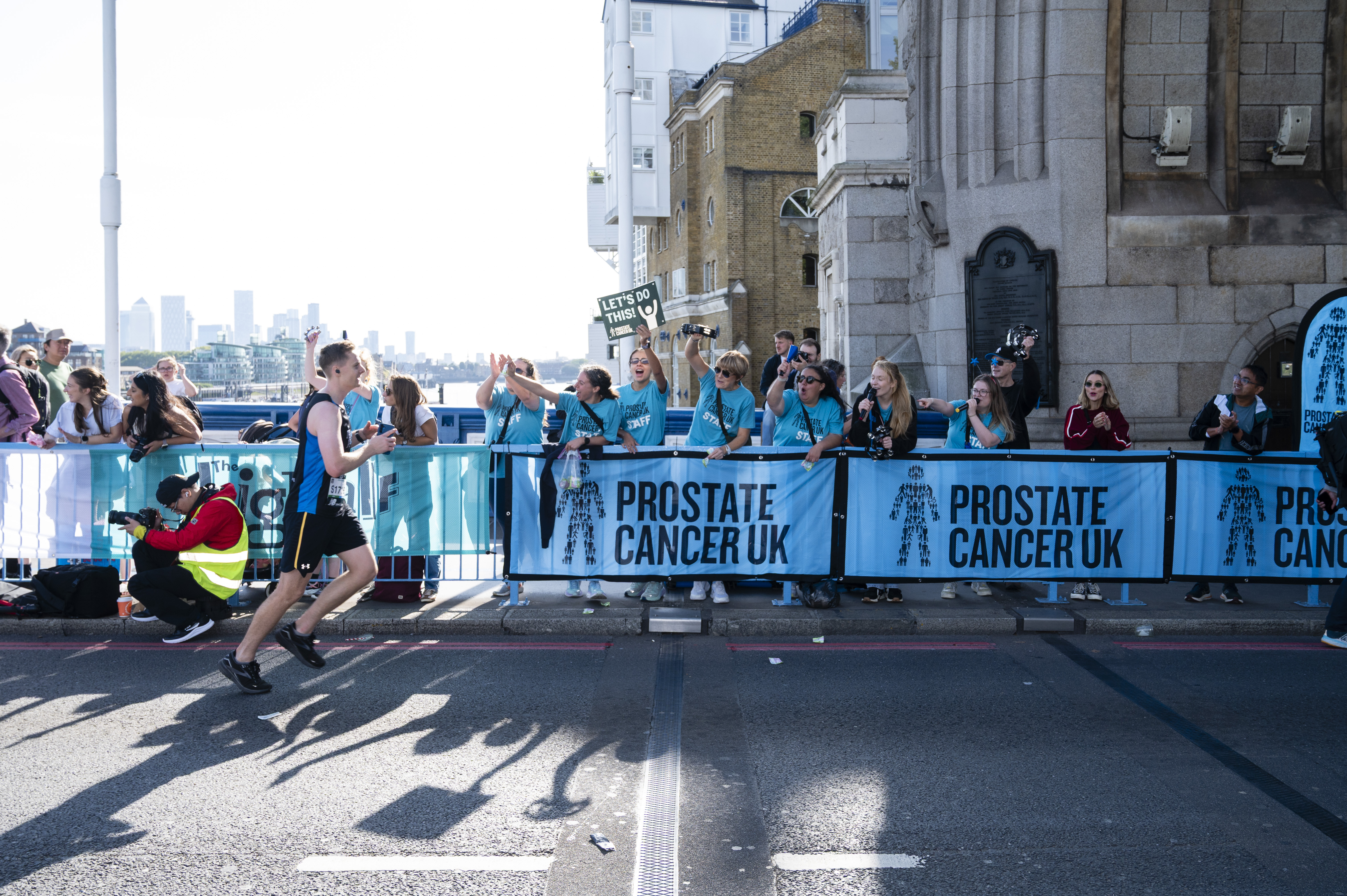 A group of people wearing blue Prostate Cancer UK t-shirts cheering on marathon runners. 