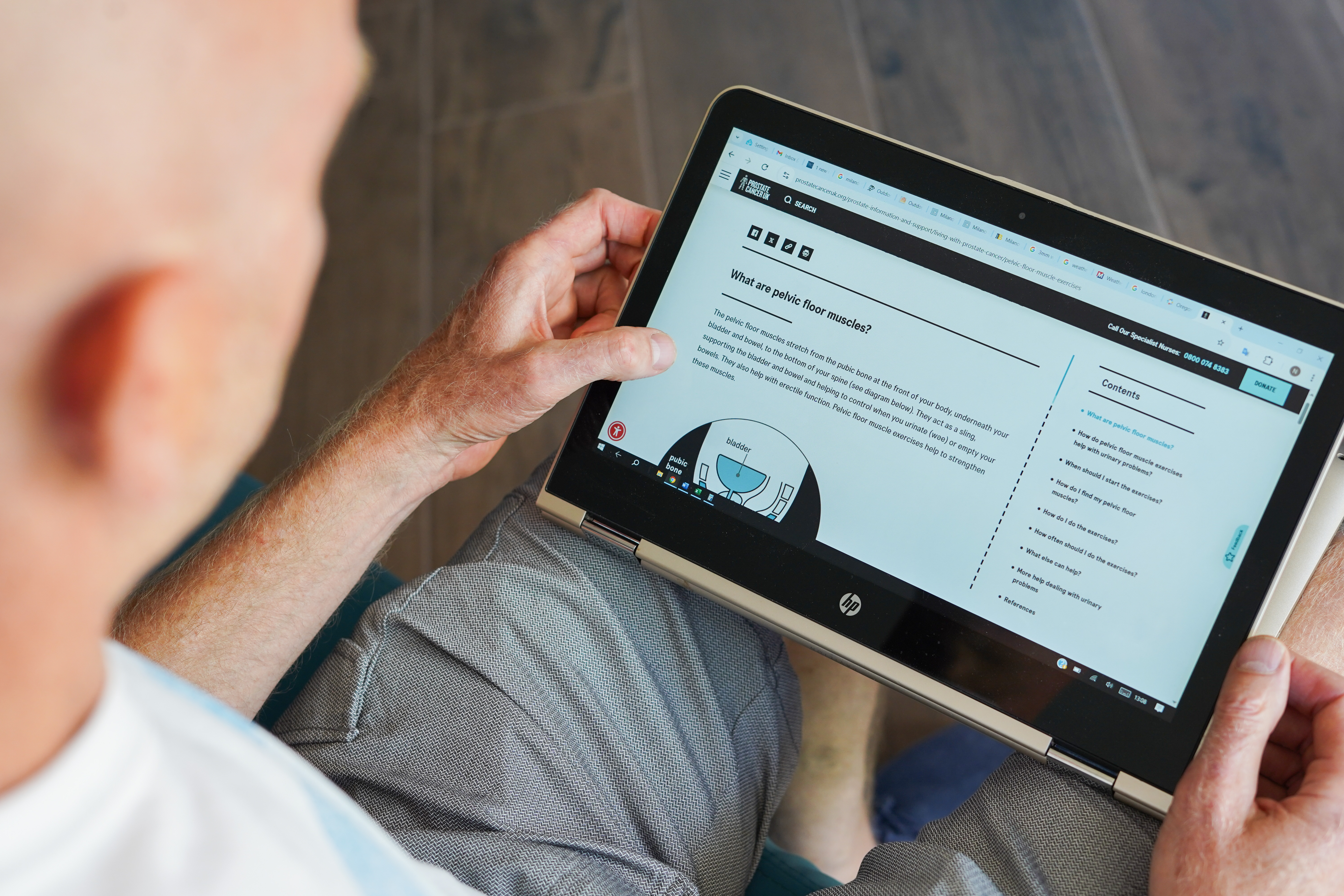 A man in a white t-shirt holding a tablet showing the Prostate Cancer UK website. 