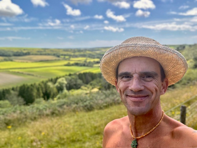 Edward wearing a straw hat standing in front of a hilly background