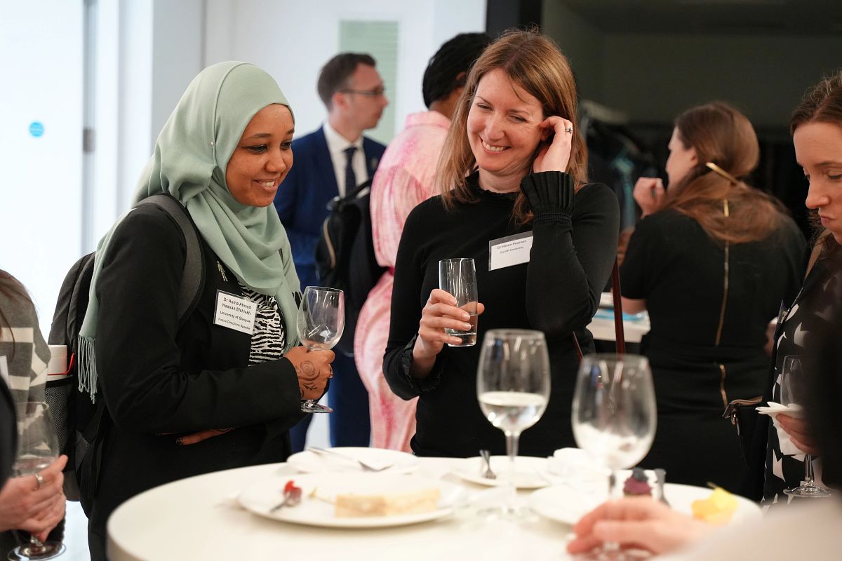 Delegates at an event holding drinks standing in front of a table, smiling and talking