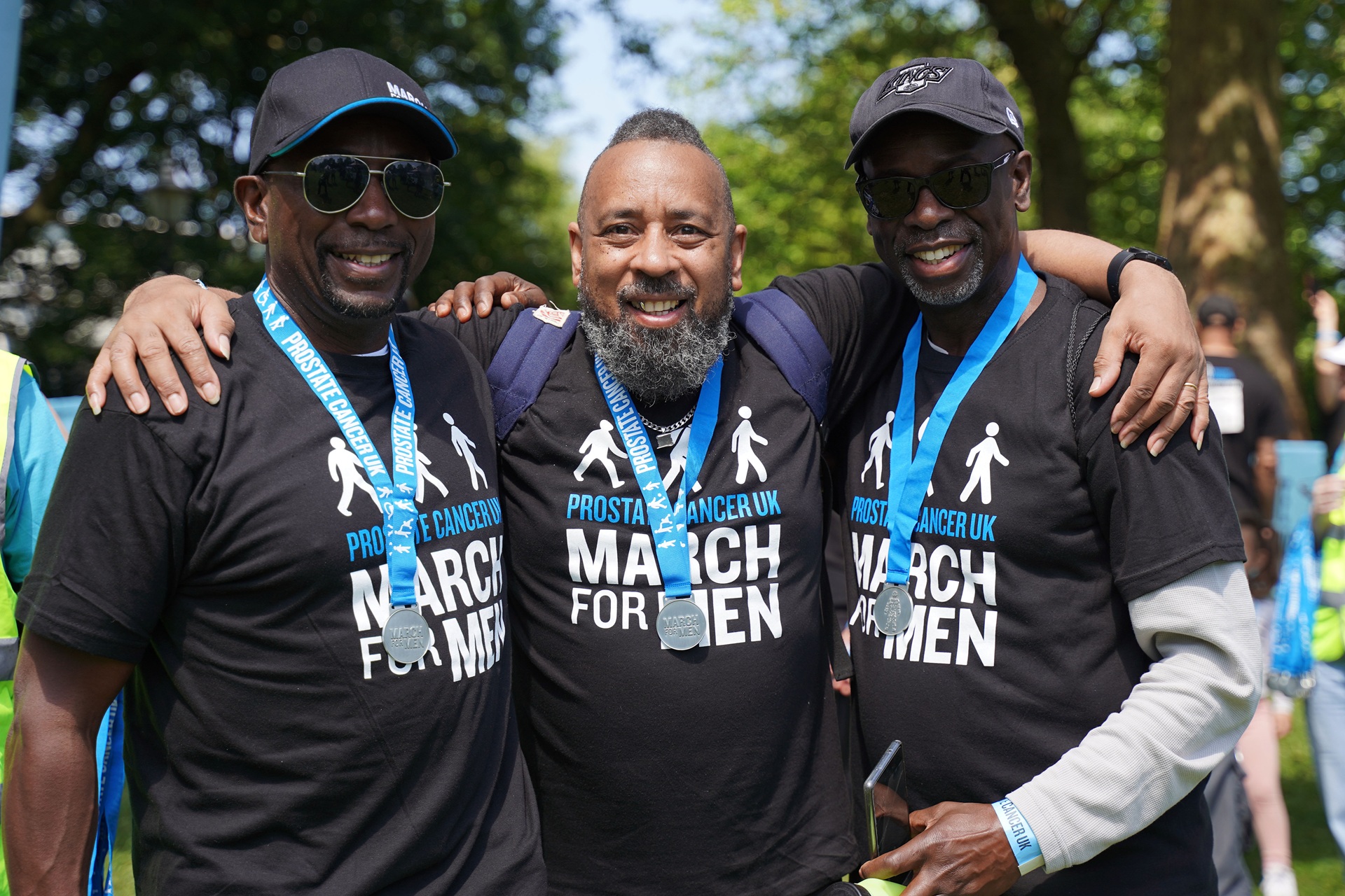 Three men stand arm-in-arm wearing medals after completing a fundraising event.