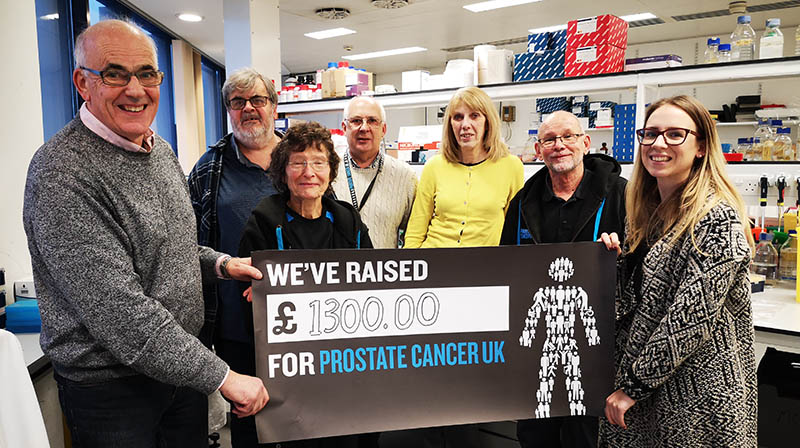 A group of people standing holding a cheque while smiling at the camera.  