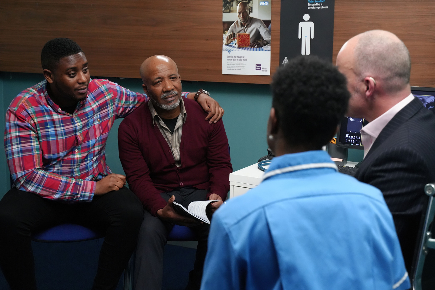 A GP and a nurse talking to an older man and a younger man in a doctor's surgery.