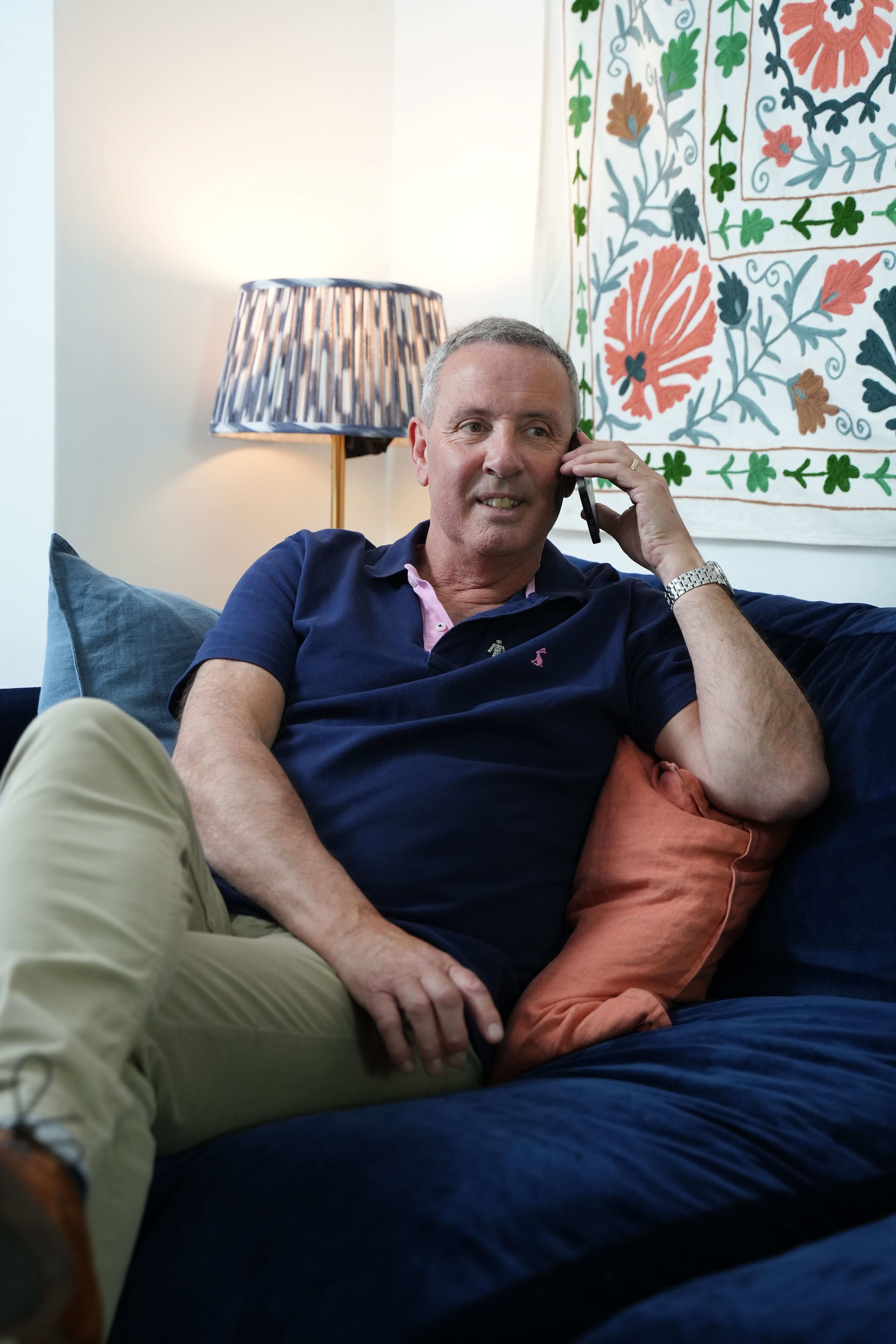 A man wearing a blue shirt sitting on a sofa and talking on the phone. 