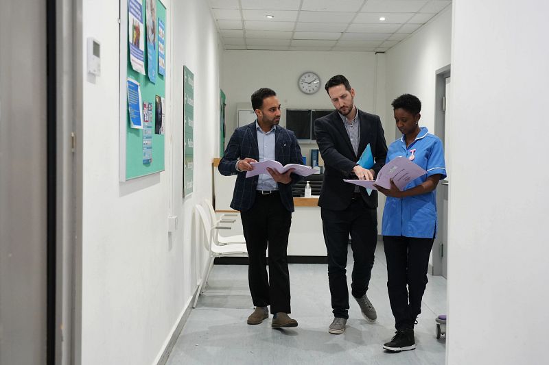 Three medical professionals walking along a corridor talking and looking at some paperwork