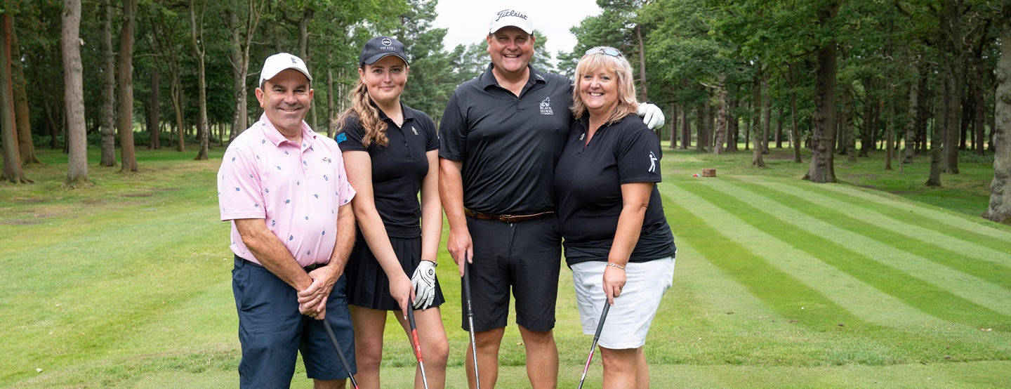 Four people in golf kit - two men and two women - standing arm in arm on a golf course.