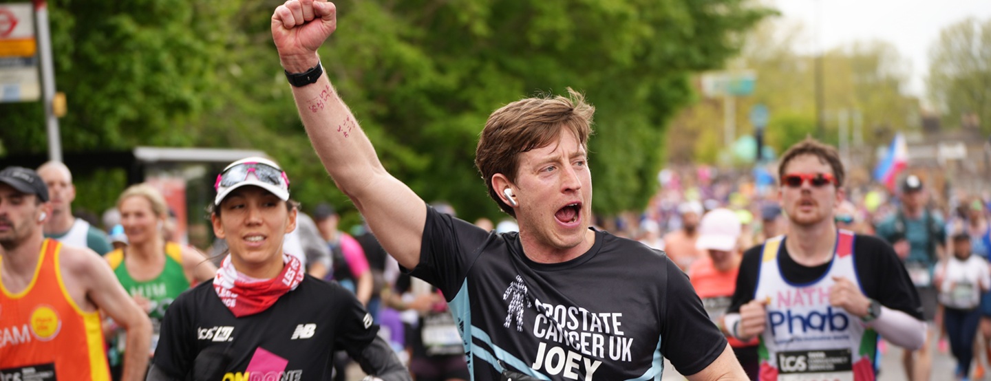 A group of runners with a man in the middle wearing a Prostate Cancer UK running top and cheering