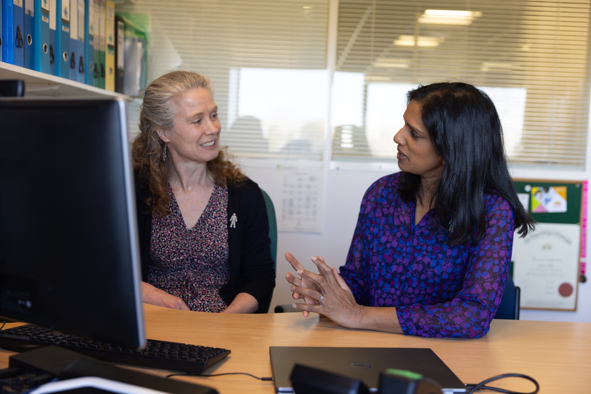 Two women sitting side by side at a computer talking