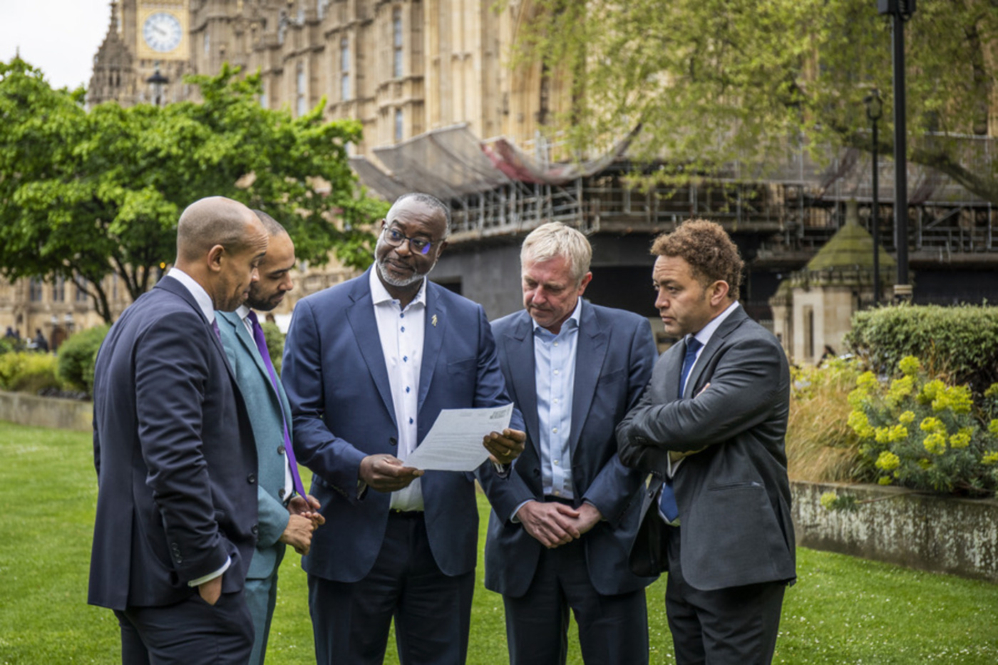 Five men wearing suits standing close together reading a letter about changing the NHS guidelines for how GPs talk about prostate cancer.