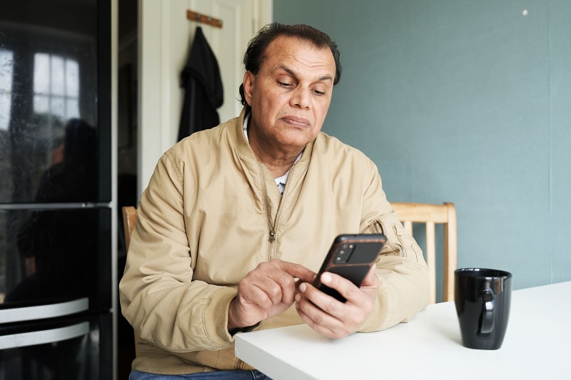 A man wearing a beige jacket sitting down and looking at his phone. 