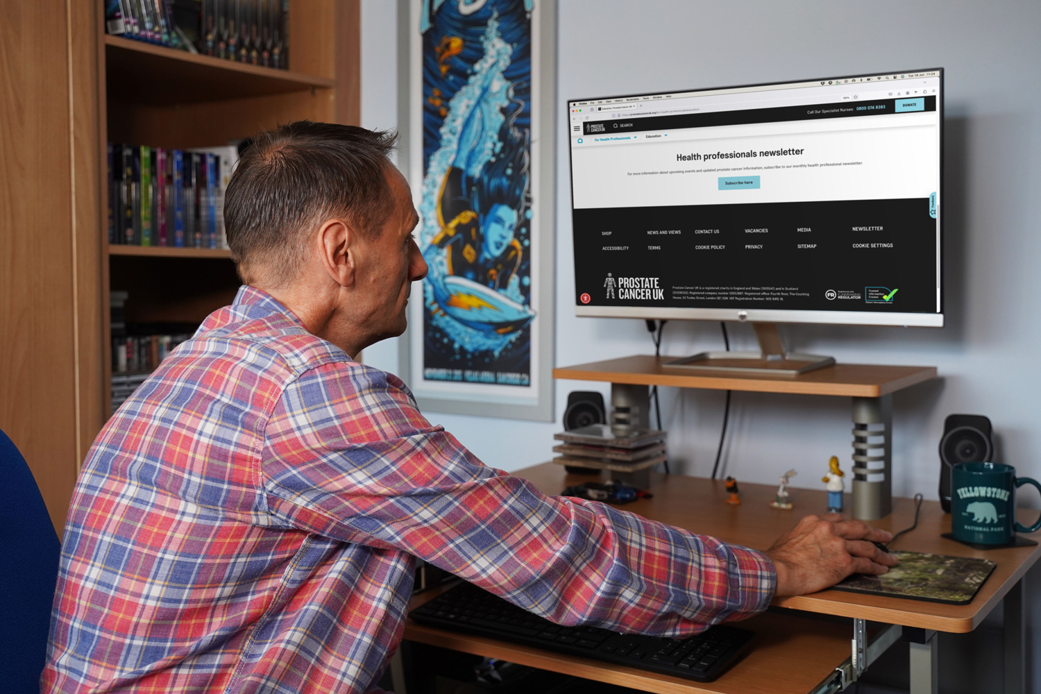 A man wearing a red shirt reading the Prostate Cancer UK website on a computer. 