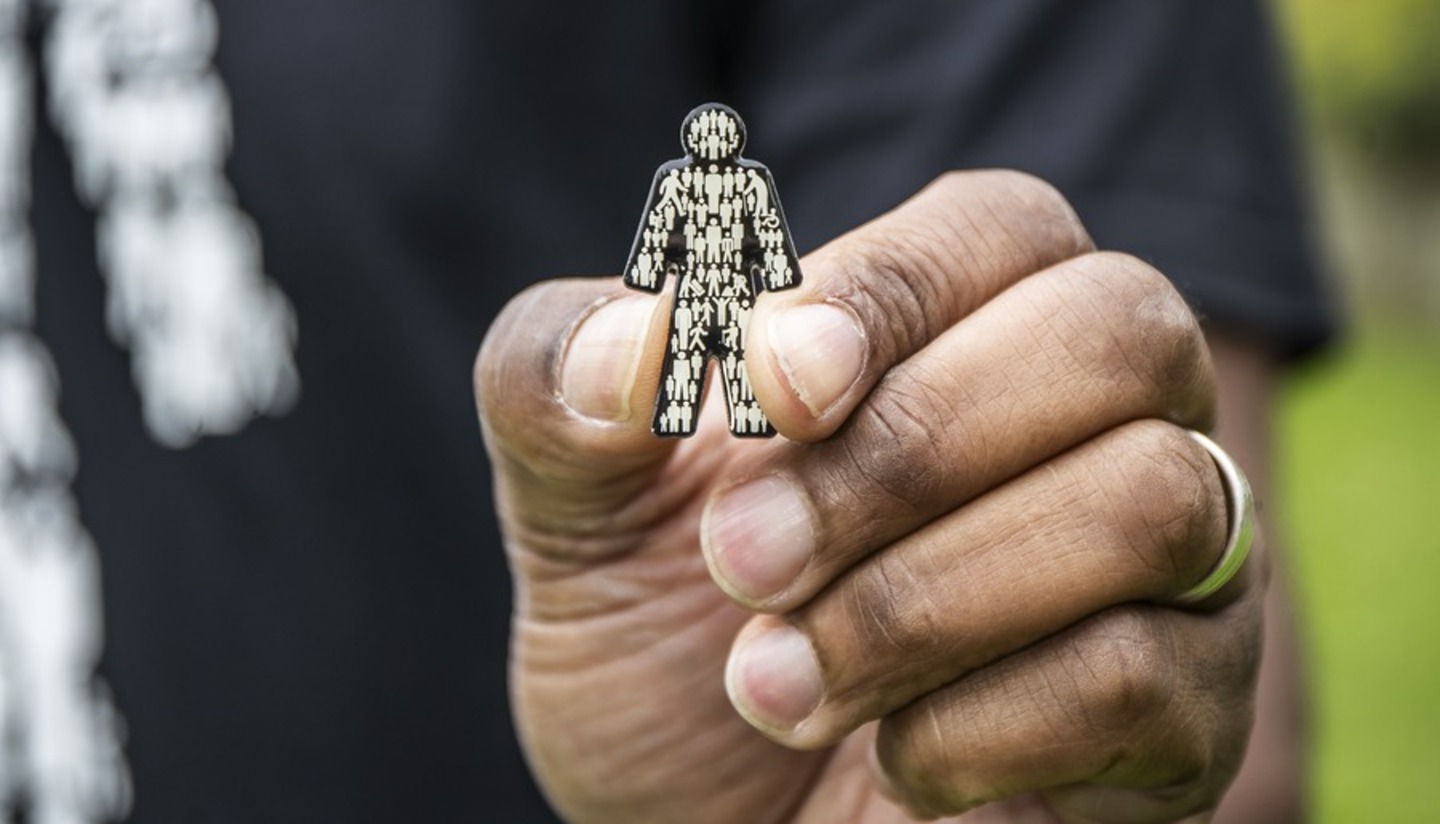 A close up of a man's hand holding up a Prostate Cancer UK 'Man of Men' badge