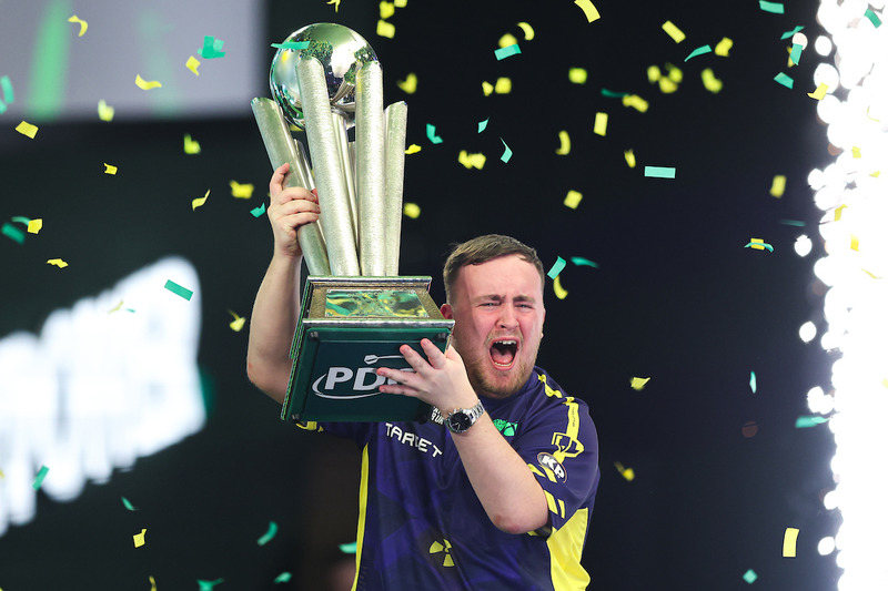 Luke Littler lifts the Sid Waddell trophy as green and gold confetti falls around him