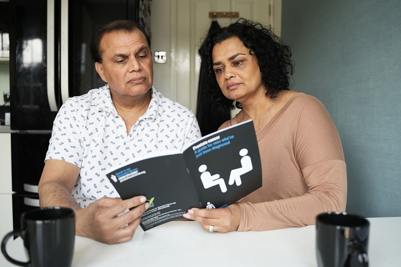 A man and woman sitting down and reading a Prostate Cancer UK booklet. 