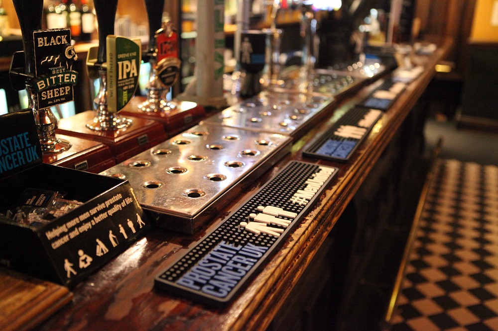 A wooden bar at a pub with Prostate Cancer UK merchandise