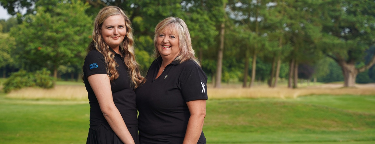 A smiling mum and daughter wearing standing on a golf course wearing black golfing kit.