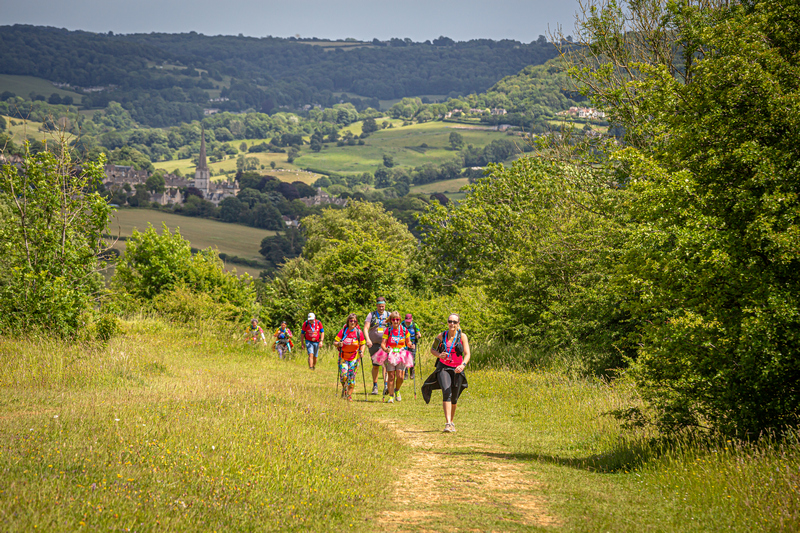A group of adults walking along a path in a field with a hilly landscape in the background