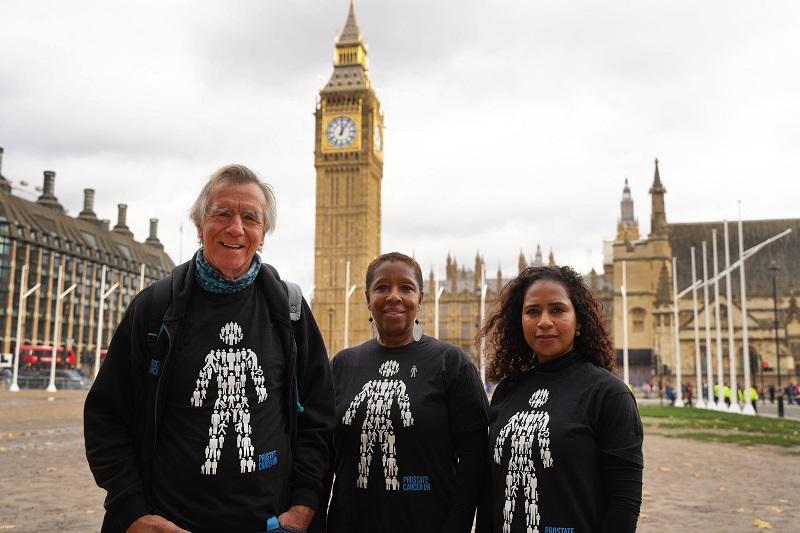 Three volunteers smiling and standing in front of the Palace of Westminster. 