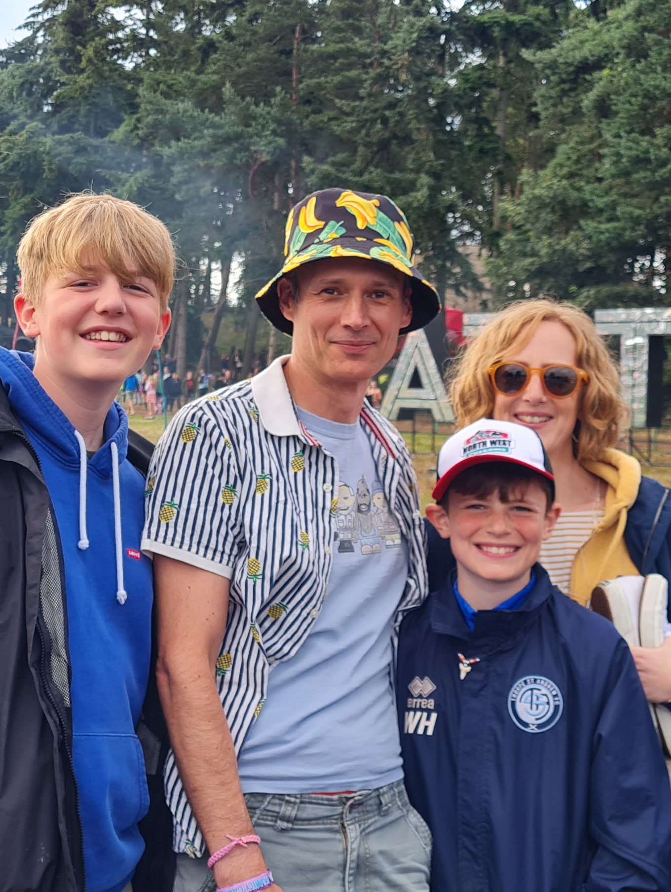 A man, woman and two boys standing together outdoors wearing raincoats smiling