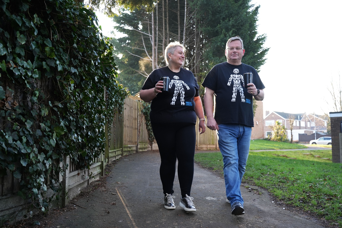 A man and woman wearing Prostate Cancer UK tee-shirts walking along a pavement