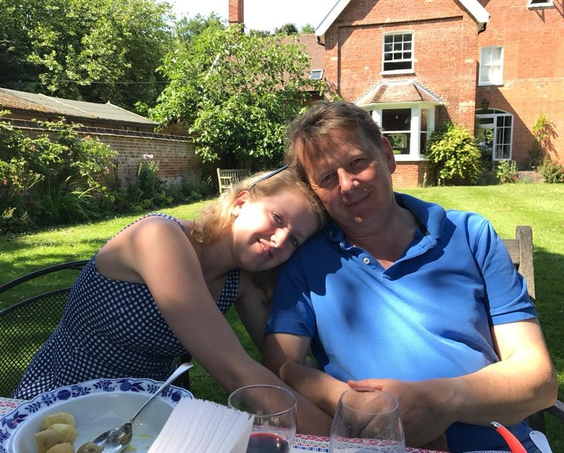 A young woman rests her head on her father's shoulder, while sitting in a garden on a sunny day.