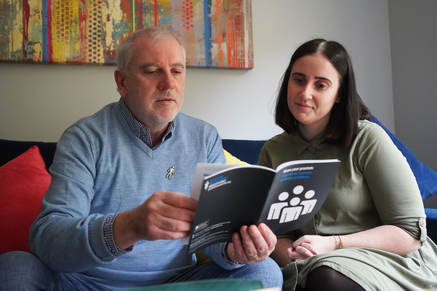 A man and woman sitting down and reading a Prostate Cancer UK booklet. 