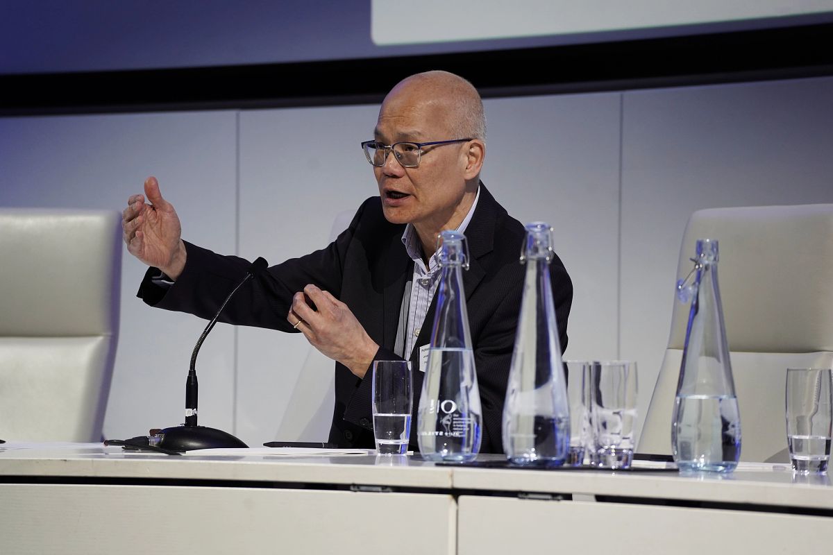 A man wearing glasses speaking into a microphone at an event