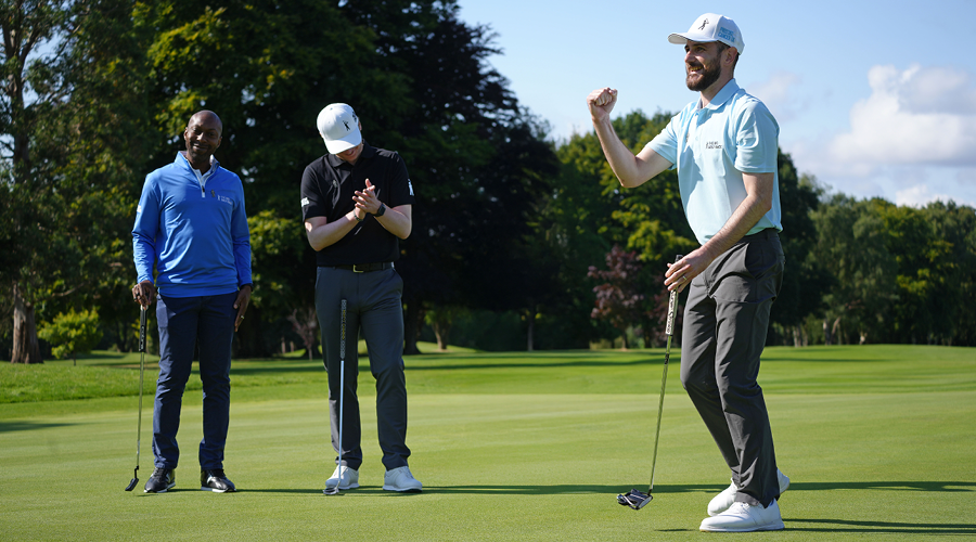 A man playing golf punches the air while two other golfers applaud him.