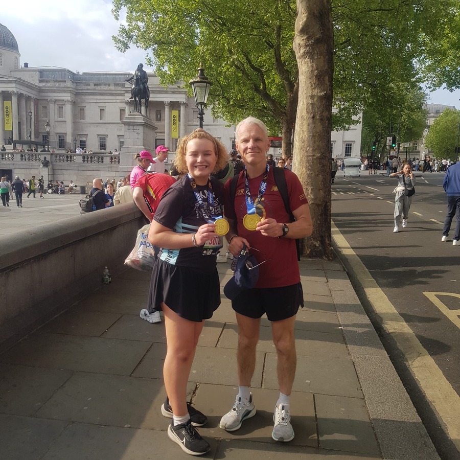 A man and a young woman wearing black Prostate Cancer UK running kit and holding their Marathon medals.
