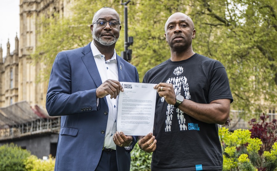 Two Black men holding up a letter between them, stood in front of the Houses of Parliament