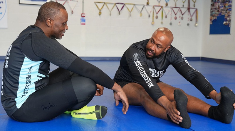 Two men at a gym sitting on the floor stretching, wearing Prostate Cancer UK exercise clothes