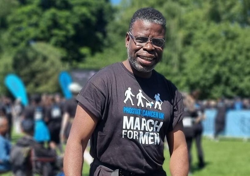 A man wearing glasses and a black t-shirt standing in a tree-lined park