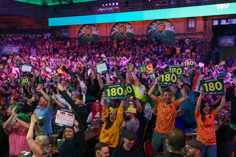 A crowd stand and cheer holding 180 signs at the World Darts Championship at Alexandra Palace.