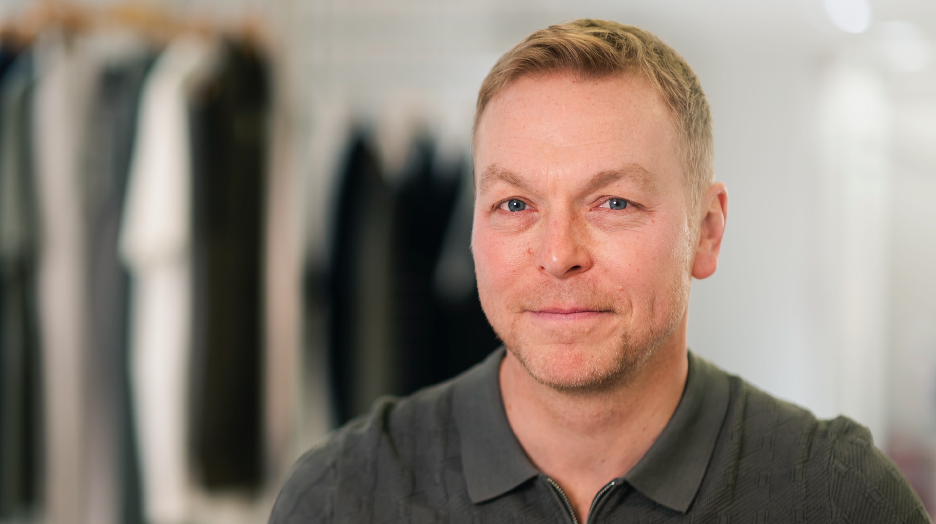 A man with blonde hair wearing a grey polo neck sweater