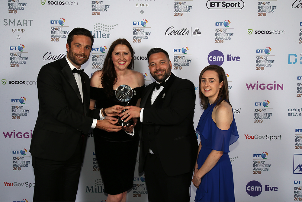 Two men and two women wearing black tie dress celebrate after receiving an award.