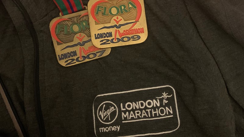 Two London Marathon medals hanging from a man's neck over a London Marathon t-shirt.